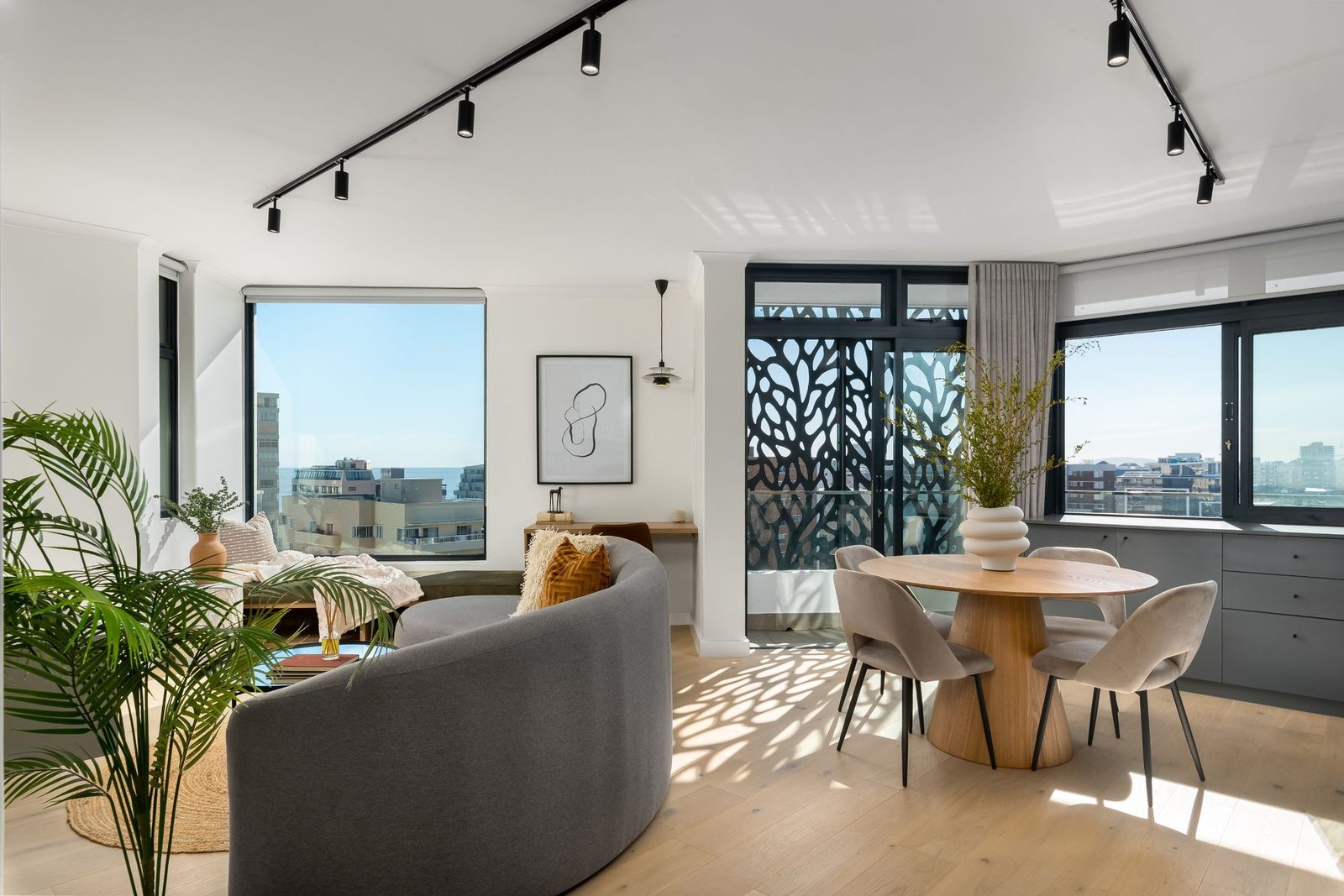 The Sage: living and dining room with black track lighting, a curved grey sofa and a patterned screen